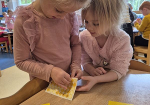 Dziewczynka odkleja naklejkę, druga dziewczynka czeka na swoją kolei z wyciągniętą ręką