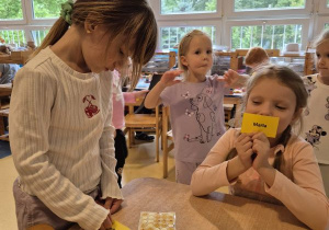 Dziewczynka nakleja naklejkę określającą jej nastrój na swoją wizytówkę, druga dziewczynka siedzi obok ze swoją wizytówką