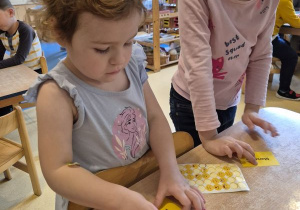 Dziewczynka nakleja naklejkę określającą jej nastrój na swoją wizytówkę, obok stoi druga dziewczynka ze swoją wizytówką