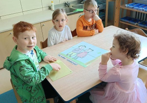Dzieci siedzą przy stoliku i układają obrazek z rozsypanki oraz dobierają do niego podpis