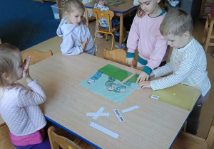 Dzieci siedzą przy stoliku i układają obrazek z rozsypanki oraz dobierają do niego podpis