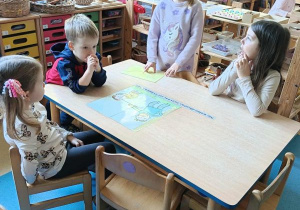 Dzieci siedzą przy stoliku i układają obrazek z rozsypanki oraz dobierają do niego podpis