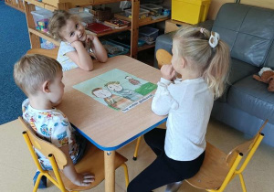 Dzieci siedzą przy stoliku i układają obrazek z rozsypanki oraz dobierają do niego podpis