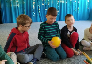 Dzieci siedzą w kręgu i podają sobie piłkę z rąk do rąk