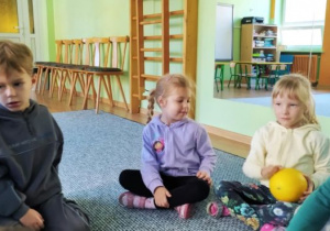 Dzieci siedzą w kręgu i podają sobie piłkę z rąk do rąk