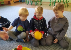 Dzieci siedzą w kręgu i podają sobie piłkę z rąk do rąk