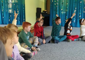 Dzieci siedzą w kręgu i podnoszą ręce do góry zgłaszając się do odpowiedzi