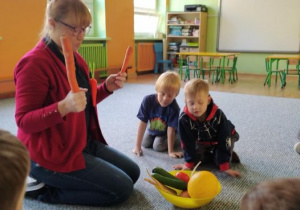 Prowadząca zajęcia trzyma w ręku marchewki oraz tłumaczy dzieciom znaczenie warzyw w diecie