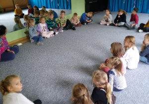 Dzieci siedzą w kręgu i słuchają prowadzącej zajęcia