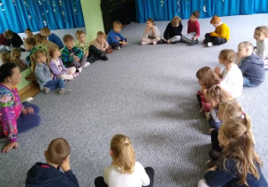 Dzieci siedzą w kręgu i słuchają prowadzącej zajęcia