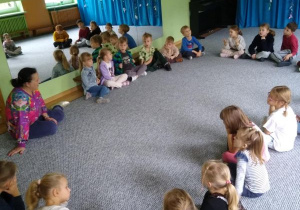 Dzieci siedzą w kręgu i słuchają prowadzącej zajęcia