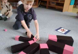 Chłopiec dokłada elementy różowej wieży i brązowych schodów do kompozycji