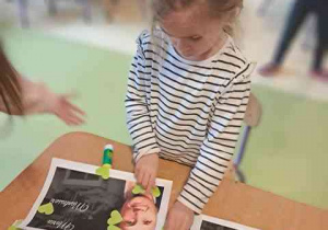 Dziewczynka dokleja elementy kolorowego papieru do swojej pracy plastycznej