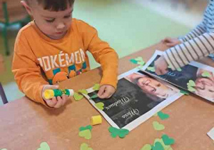 Chłopiec dokleja elementy kolorowego papieru i tworzy ramkę do portretu Marii Montessori