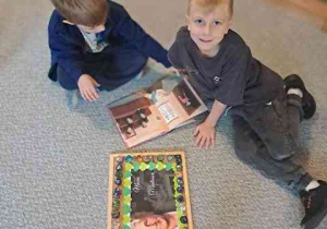 Chłopcy oglądają książkę o Marii Montessori, obok leży podkładka z portretem Marii Montessori