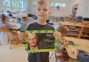 Chłopiec prezentuje wykonaną przez siebie ramkę z elementów kolorowego papieru do portretu Marii Montessori