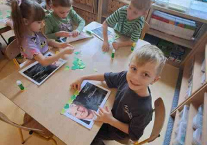 Dzieci przy stoliku podczas wyklejania ramki z elementów kolorowego papieru do portrertu Marii Monttessori