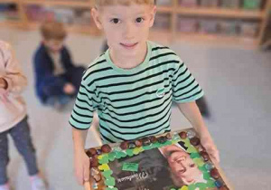 Chłopiec trzyma w dłoniach podkładkę z portretem Montessori do którego układał ramkę z kasztanów i kamieni