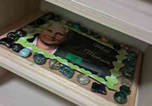 Kompozycja położona na wystawie przed salą przedstawiająca portret Marii Montessorii z utworzoną przez dziecko ramką z elementów kolorowego papieru oraz kamieni