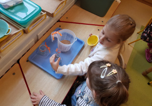 Dziewczynki przesypują piasek.