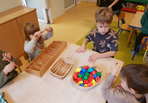 Dzieci siedzą przy stole, na którym znajdują się pomoce dydaktyczne.