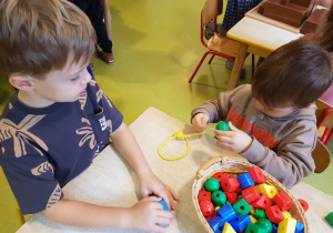 Chłopcy nawlekają korale na sznurek.