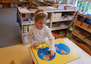 Dziewczynka układa drewniane puzzle z kontynentami.