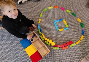 Jaś buduje z klocków i kolorowych cylindrów.