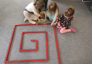 Dzieci układają labirynt z wykorzystaniem czerwonych sztang.