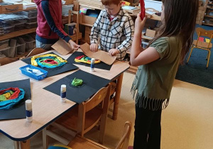 Dzieci stoją przy stoliku i wykonują pracę plastyczną - ślimaka