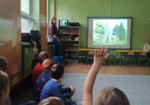 Dzieci oglądają zdjęcia wyświetlane na tablicy interaktywnej, jedno z dzieci podnosi rękę do góry