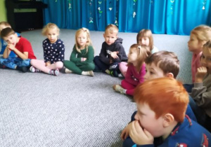 Dzieci siedzą w kręgu i słuchają prowadzącej zajęcia