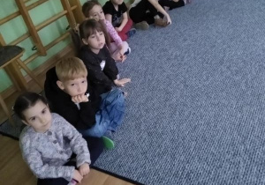 Dzieci siedzą w kręgu i słuchają prowadzącej zajęcia