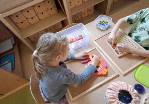 Dzieci siedzą przy stoliku i wykonują indywidualne ćwiczenia z zakresu edukacji matematycznej poprzez montessoriański materiał rozwojowy