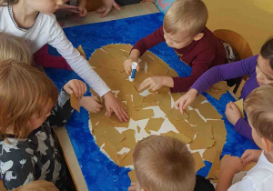 Dzieci wyklejają kawałkami papieru kształt renifera