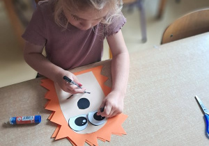 Dziewczynka rysuje uśmiech na swojej pracy plastycznej przedstawiającej jeża