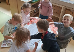 Dzieci przy stoliku w czasie malowania farbami sylwety jeża na dużym arkuszu