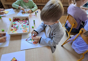 Dzieci w czasie pracy plastycznej wyklejają elementami kolorowego papieru szablon liścia
