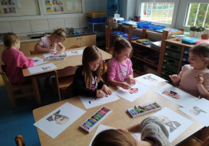 Dziewczynki siedzą przy stole i rysują Janusza Korczaka