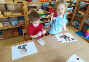 Dzieci siedzą przy stoliku i ozdabiają serduszkami portret Janusza Korczaka