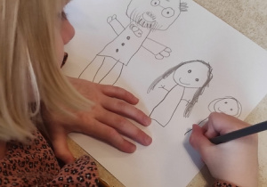 Dziewczynka rysuje Janusza Korczaka z dziećmi.