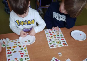 Chłopcy przyklejają na talerzyki owoce i warzywa