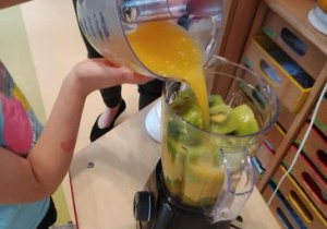 Dziewczynka wlewa świeżo wyciśnięty sok pomarańczowy do blendera