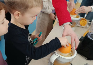 Chłopiec wyciska sok z pomarańczy z pomocą osoby prowadzącej warsztaty