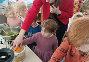 Dziewczynka wyciska sok z pomarańczy z pomocą osoby prowadzącej warsztaty