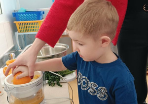 Chłopiec wyciska sok z pomarańczy z pomocą osoby prowadzącej warsztaty