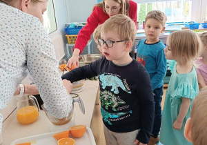 Chłopiec wyciska sok z pomarańczy z pomocą osoby prowadzącej warsztaty