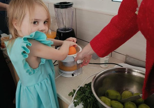 Dziewczynka wyciska sok z pomarańczy z pomocą osoby prowadzącej warsztaty