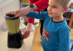 Chłopiec wyciska sok z pomarańczy z pomocą osoby prowadzącej warsztaty