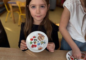 Dziewczynka prezentuje talerz z naklejkami zdrowych produktów
